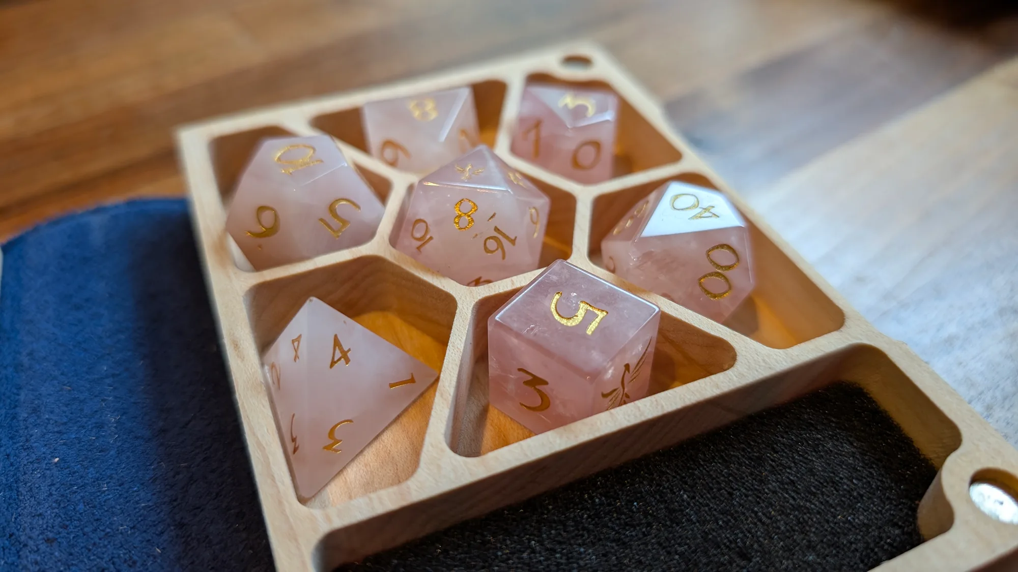 A set of rose quartz dice with gold numerals, in a wooden dice tray